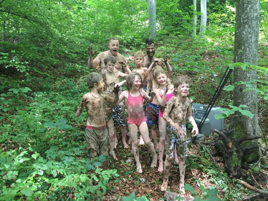 `Kinder und Betreuer mit Schlamm bedeckt lachen im Wald, Abenteuerkurs Dakawo`