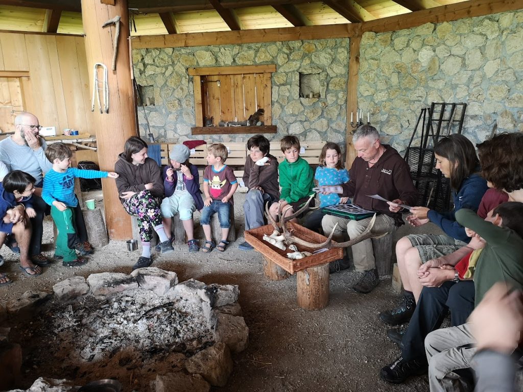 Kinder beim Naturkurs in der Hütte mit Kursleiter, Natur- und Wildnisschule Dakawo Schweiz