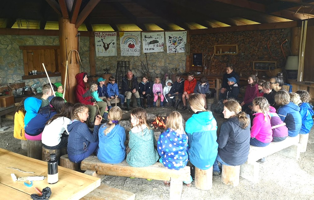 Kinder sitzen im Kreis ums Feuer beim Abenteuerlager, Natur- und Wildnisschule Dakawo Schweiz